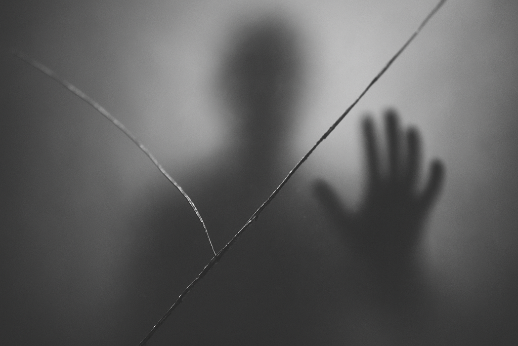 Riss im Spiegel; schemenhafte Gestalt mit ausgestreckter Hand.